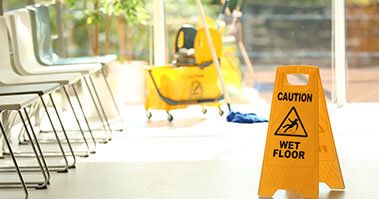 A wet floor sign and cleaning trolley next to a row of chairs