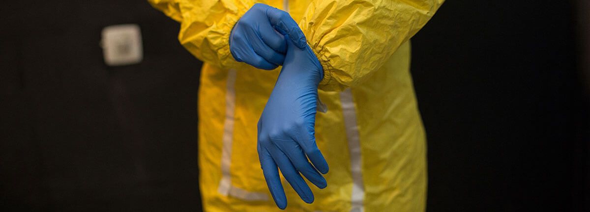A worker in a hazmat suit putting on rubber gloves.